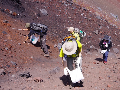 富士山の砂礫の登山道で、ごみ袋を持って清掃する環境省職員